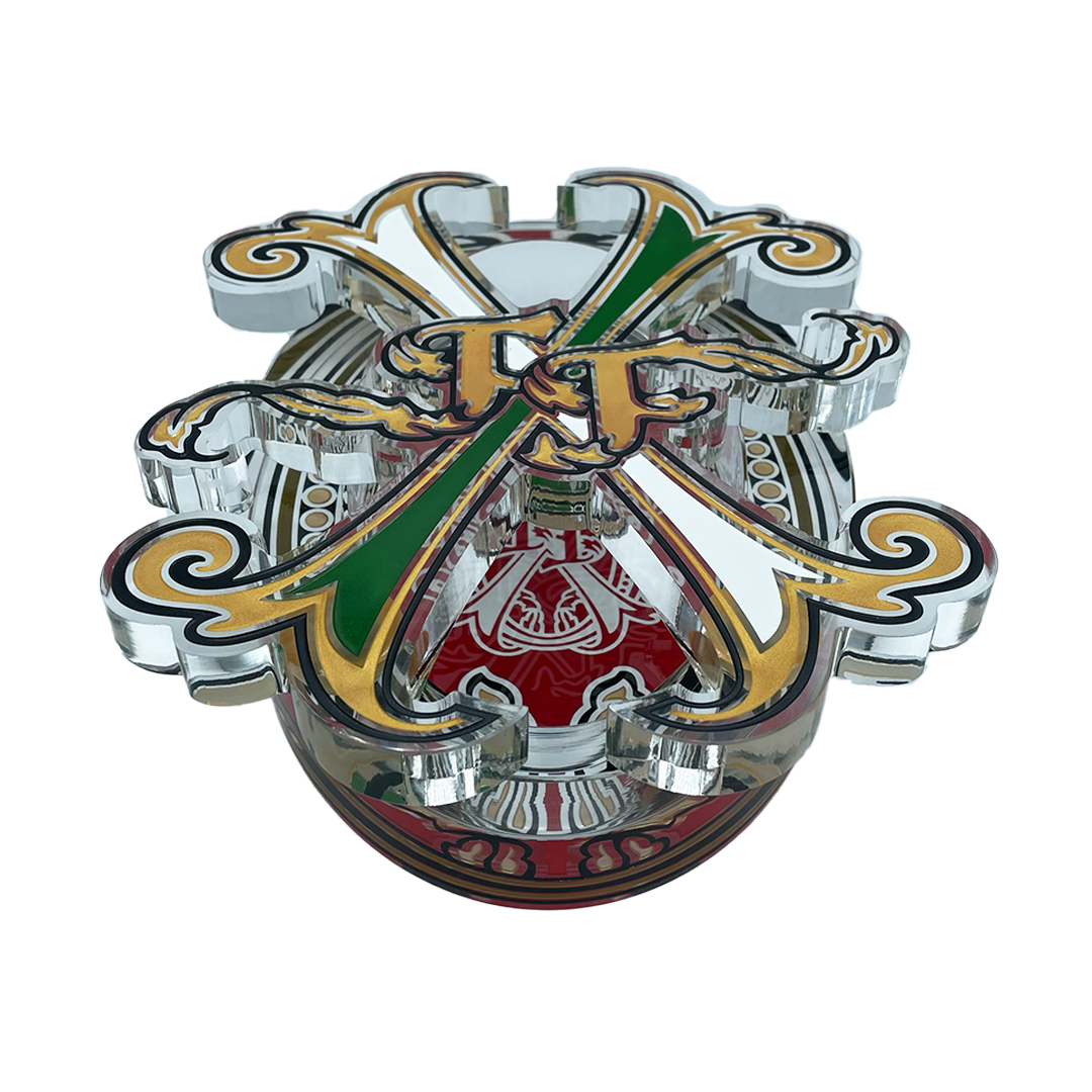 A highly detailed, chrome-plated metal toy or collectible emblem featuring crossed green and gold swords, a red central shield with white script, and ornate gold scrollwork on a white background.
